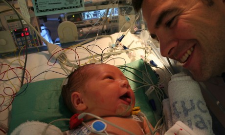 Oscar Windsor as a new born baby having cooling treatment with lots of wires around him. His father is looking at him lovingly
